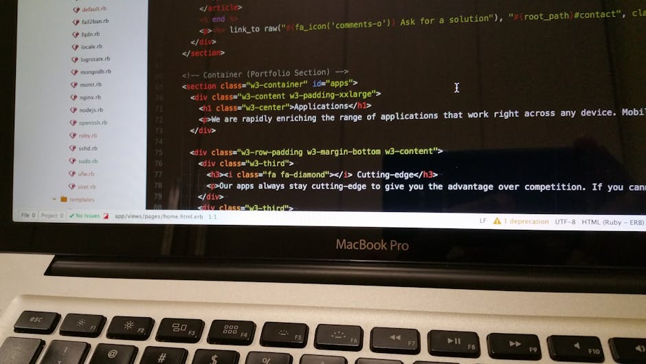 Close-up view of a MacBook Pro laptop placed on a desk, displaying a code editing software with highlighted HTML and Ruby code, related to web development. The laptop screen shows a dark background wi